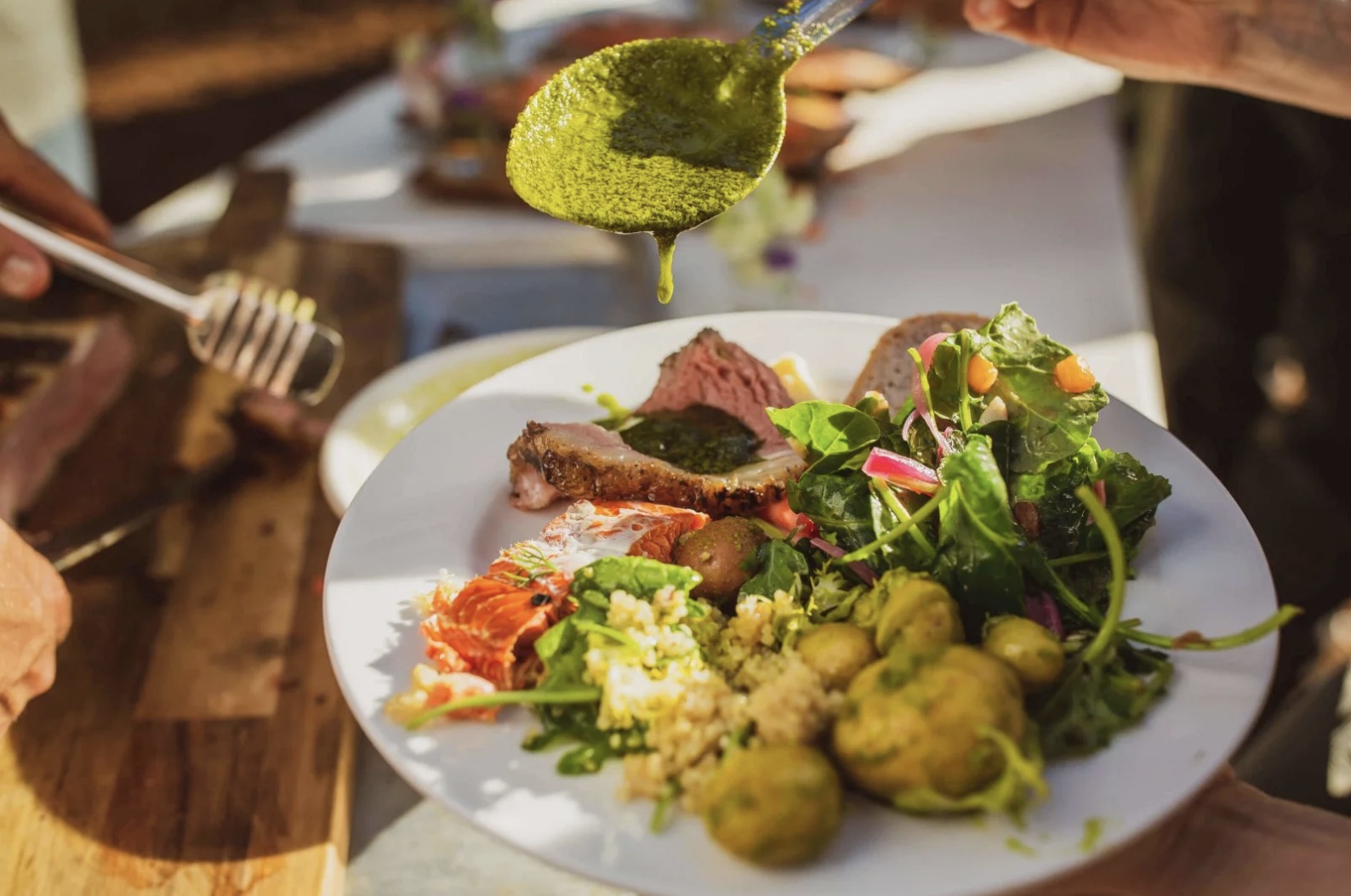A plated EATS dish being finished with herb sauce at an outdoor event